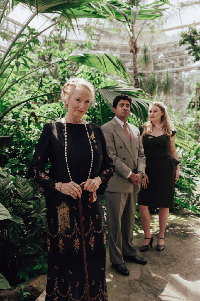 Lisa in black dress as Violet venable with Doctor and Niece in background of a tropic greenhouse.